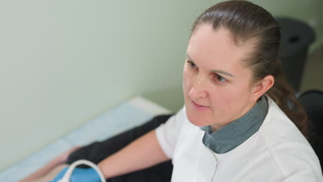 clinical laboratory scientist carefully monitors examination machine screen while moving transducer on patient lying on examination bed during diagnostic procedure in clean medical environment