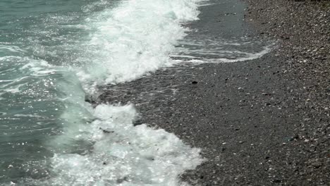 Waves-hit-the-shore-at-beach-of-Kalamata,-Peloponnese,-Greece,-slow-motion-tilt-reveal-shot