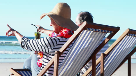 senior couple sitting on sunlounger and having cocktail at beach