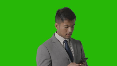 Studio-Shot-Of-Businessman-In-Suit-Against-Green-Screen-Moving-And-Using-Mobile-Phone-