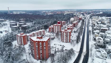 Edificios-Altos-Con-Paredes-Marrones-Cubiertos-De-Nieve-Mientras-Los-Coches-Circulan-Por-Debajo-De-La-Autopista,-Descripción-Aérea