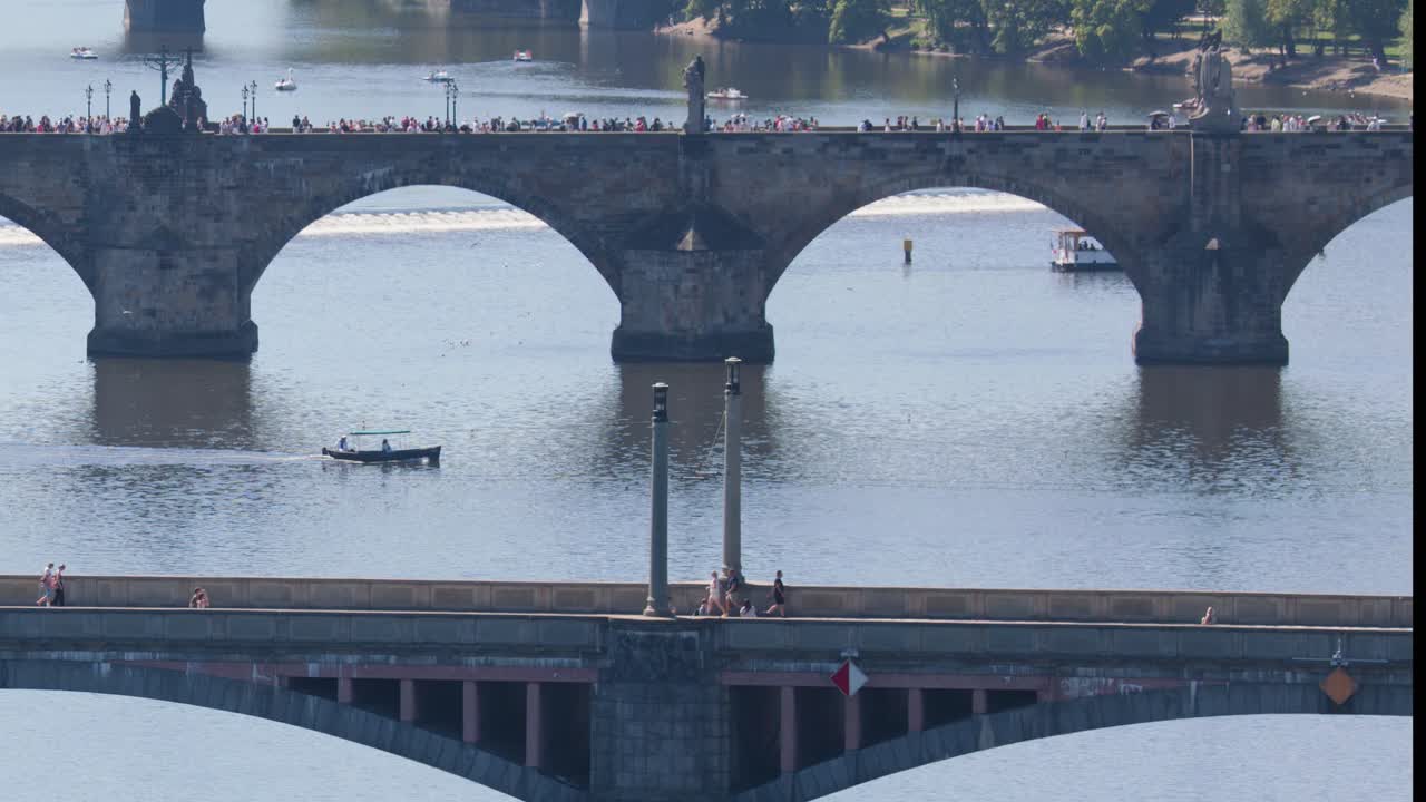 Daytime aerial pan reveals Charles Bridge, Vltava River, boats, and cityscape under clear sunlight