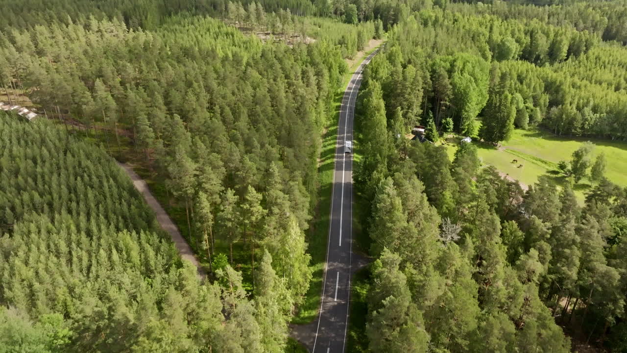 AERIAL: Clouds shadows moving over a sunny forest landscape, with a RV on a road