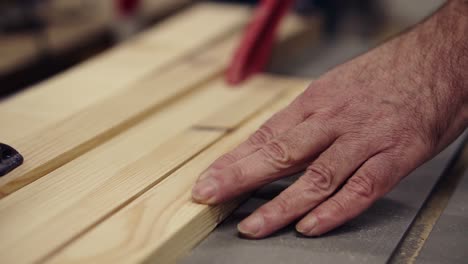 slow motion carpenter wrinkled hands cutting wooden board on saw machine. industrial machine with circular saw cuts wooden board. male hands gently pushing a pattern to a circular disk. slow motion