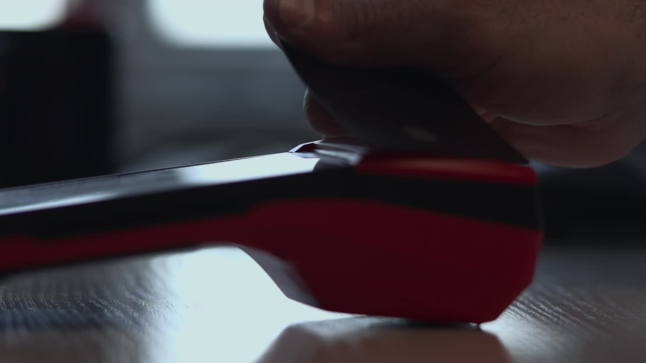 木製の机の上で光沢のある赤いワイヤレスマウスのボタンを指でタップするユーザーのクローズアップ。