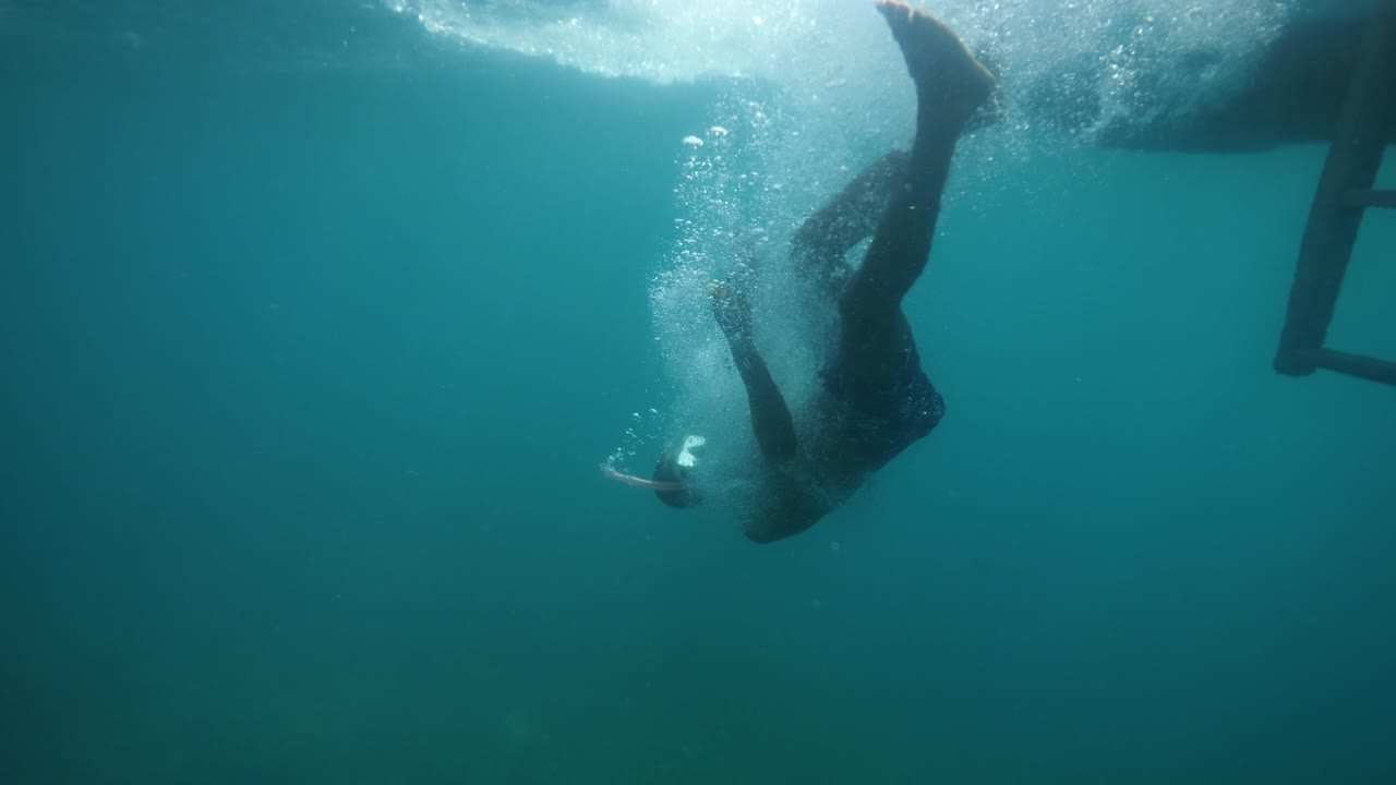 un hombre con una máscara de buceo filmando un video selfie mientras se cae de un barco