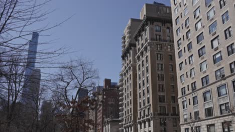 classic manhattan residential buildings rise above tree-lined streets, with a modern skyscraper towering in the background
