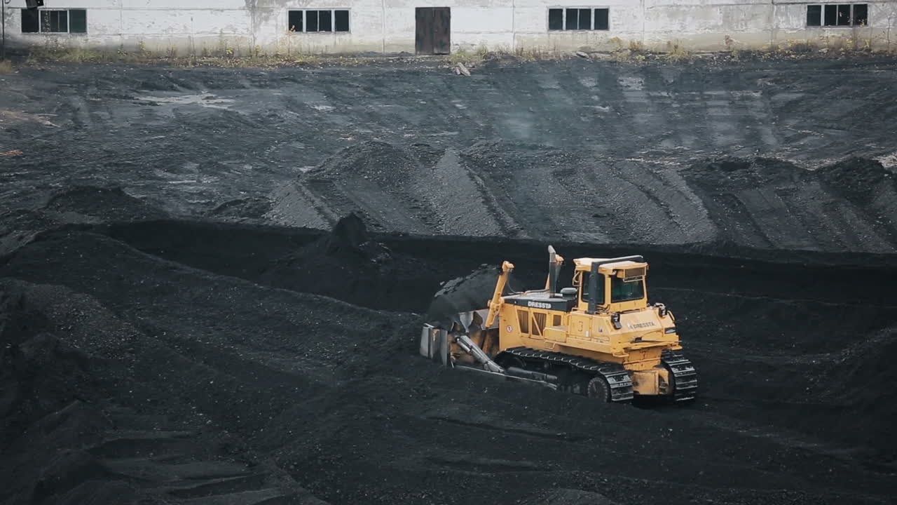 Coal mining industry and transportation. Yellow tractor riding at coal warehouse for transportation