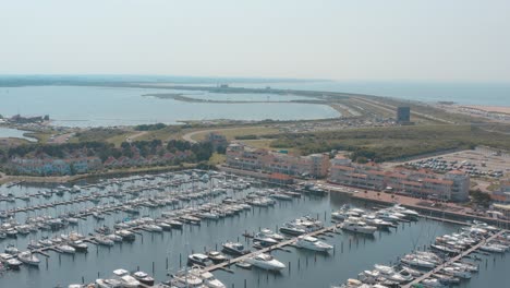 cinematic drone - aerial tracking panorama shot of a marina - port with sailing boats on a sunny day with the north sea in the background, 25p