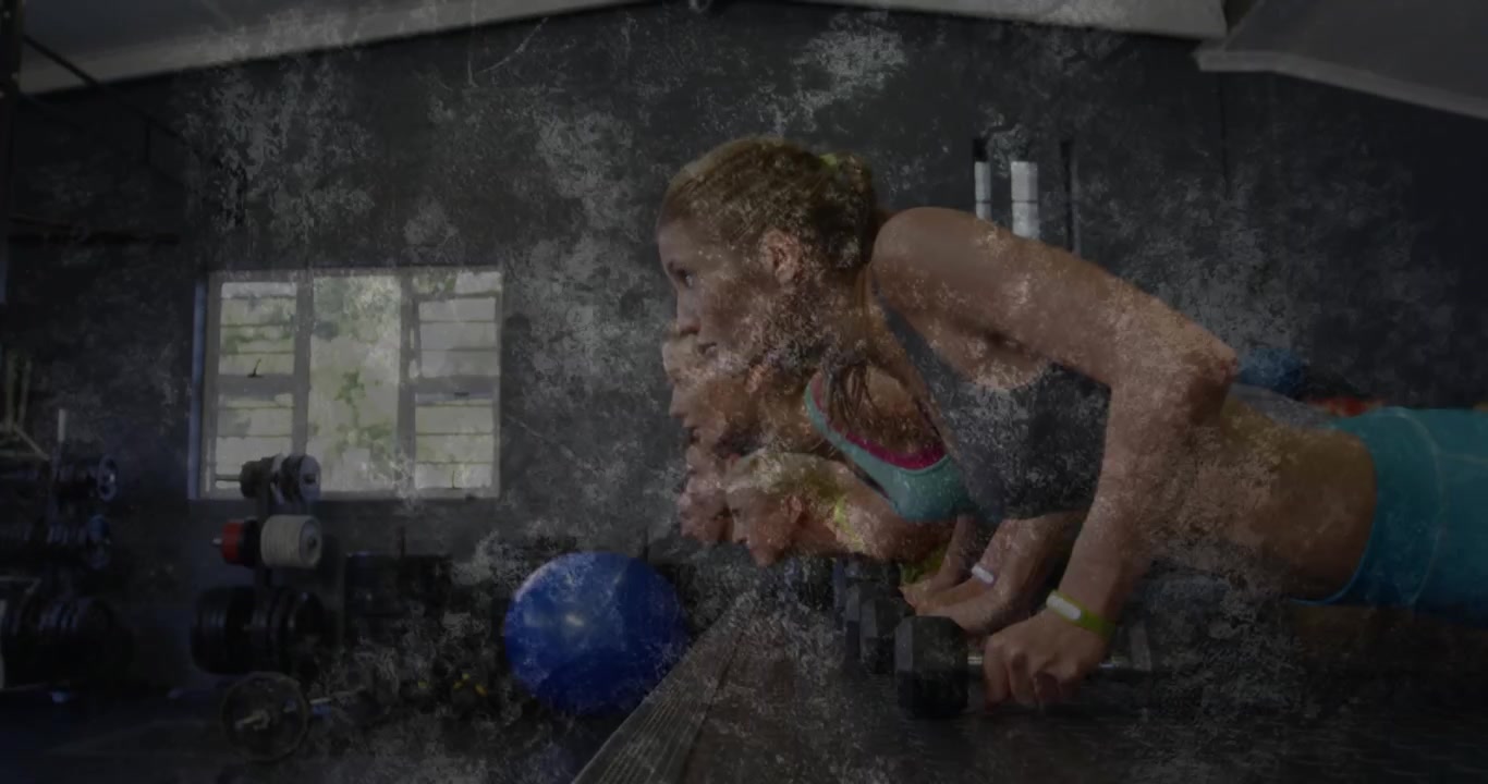 Donna in primo piano che esegue piegamenti con manubri per la forza in palestra seguendo le indicazioni dell'allenatore, grana che oscura i volti