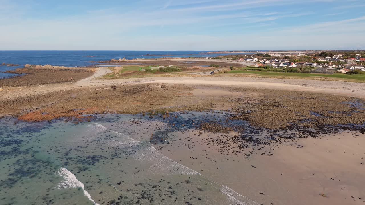 Flight over crystal clear calm waters of perfect bay with golden sand and distant views on sunny day in Guernsey