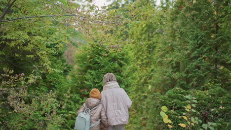 woman holding kid hand and leash walking down leafy forest steps, bundled in warm jackets and scarf, caring guidance in autumn greenery, gentle family moment of support