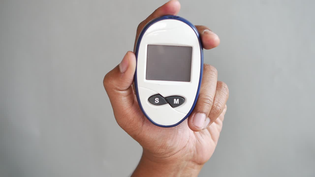 Mans hand holding a glucose meter against gray background