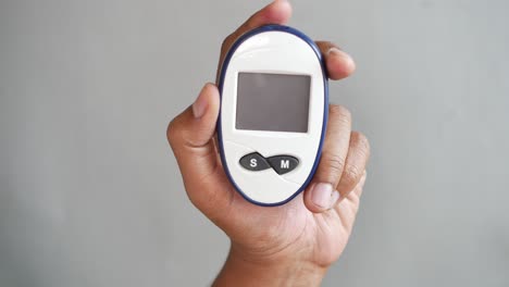 mans hand holding a glucose meter against gray background