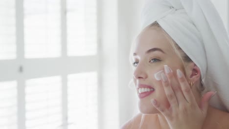 una mujer caucásica feliz de talla plus con bata de baño poniendo crema en la cara en cámara lenta.