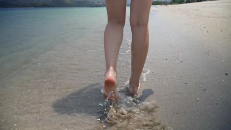 Primer-Plano-En-Cámara-Lenta-De-Piernas-Y-Pies-Femeninos-Caminando-Por-Aguas-Poco-Profundas-En-Una-Playa-Tropical