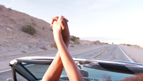 una joven pareja negra en un coche abierto con las manos en el aire