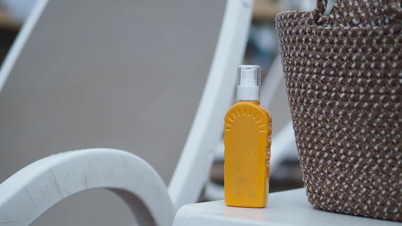 Botella de protector solar en spray y bolso de mimbre en una tumbona