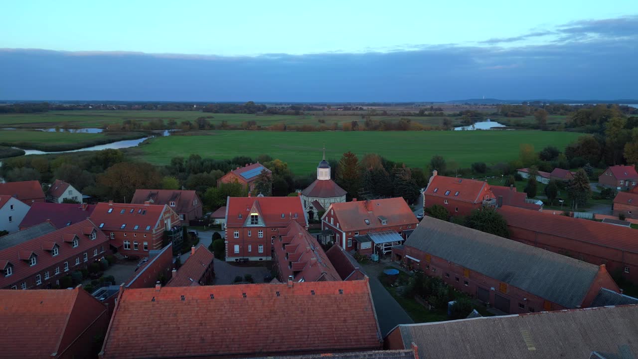 a small village illuminated by golden hour light, casting long shadows over the surrounding fields. Fantastic aerial view flight drone shot footage from above