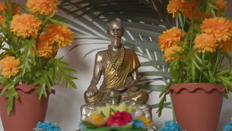 buddhist statue on a shelf in between orange flowers