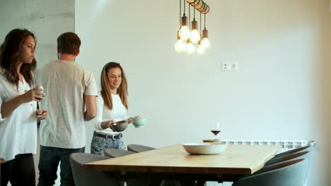 Smiling-friends-putting-snacks-and-glasses-with-red-wine-on-table