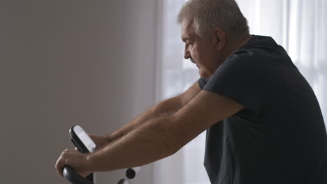 training-on-stationary-bike-for-health-of-cardiovascular-system-middle-aged-man-is-doing-exercises-for-good-physical-condition-portrait-shot