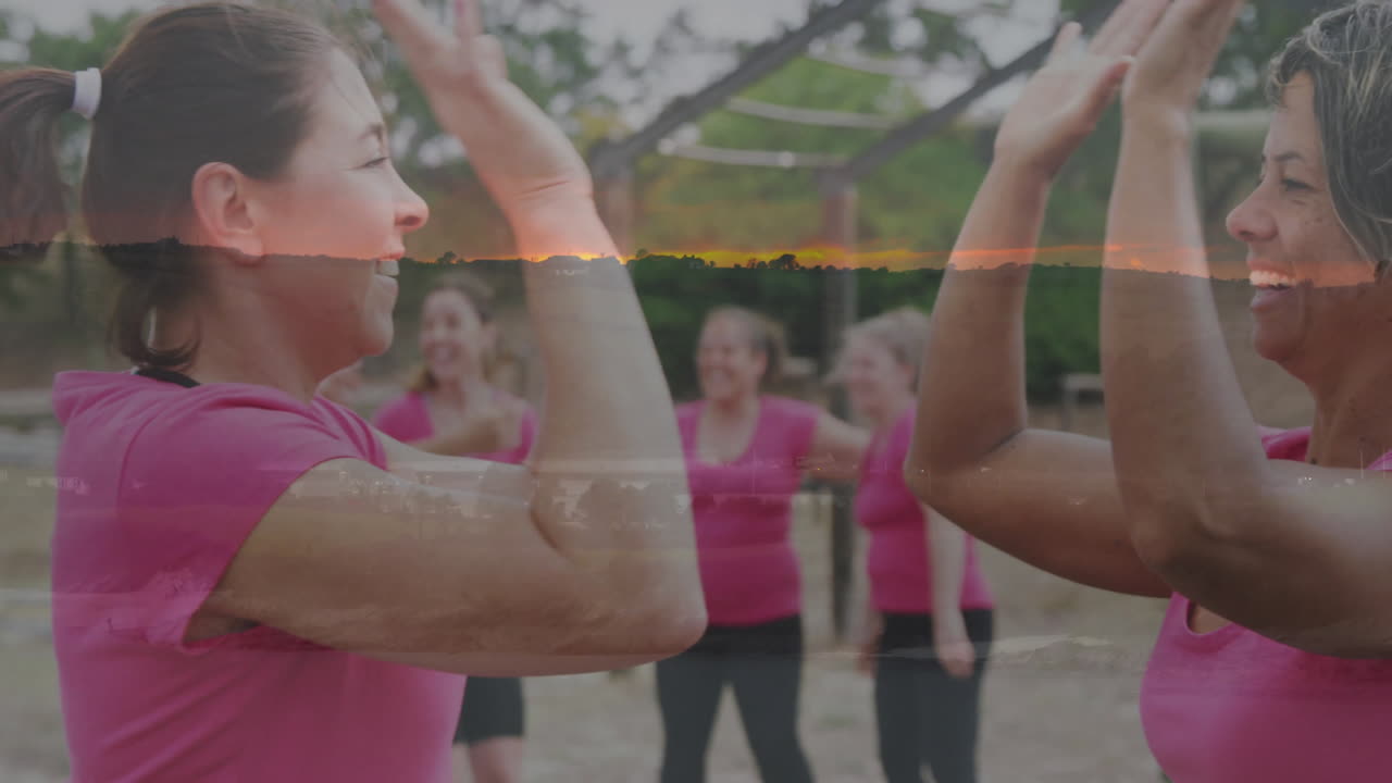 High-fiving outdoors, women in pink shirts celebrating with sunset animation overlay
