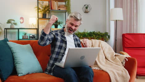 successful happy senior man using laptop check e-mail read unbelievable good offer celebrate victory