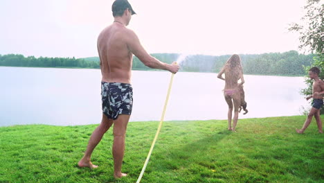 Sunny-summer-day-on-the-lawn-family-with-two-children-have-fun-playing-with-water-and-laughing.-Cheerful-atmosphere-of-a-happy-family