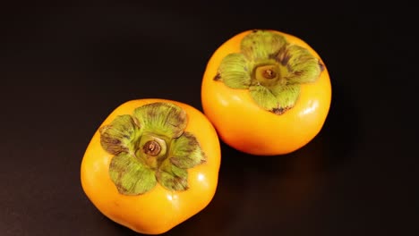 two persimmons rotating on a dark background