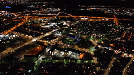 Aerial-view-overlooking-the-illuminated-cityscape-of-Reykjavik,-night-in-Iceland