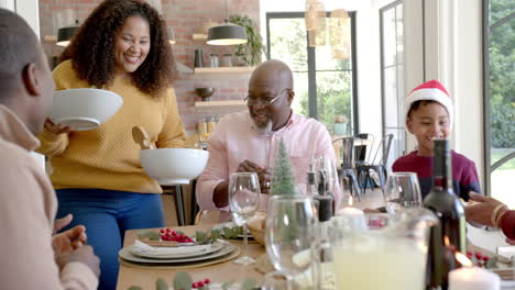 happy african american mother serving dishes to multi generation family at christmas dinner table