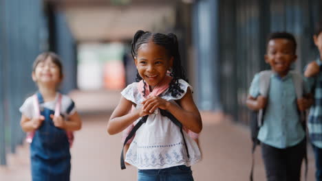 portrait of multi-cultural elementary school pupils with backpacks on walkway outdoors at school