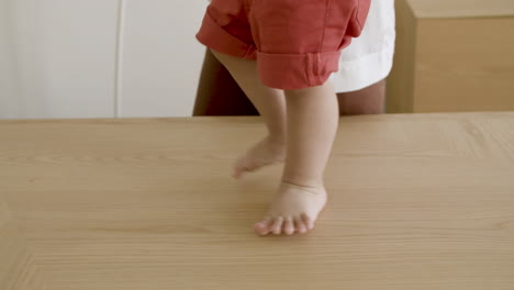 close-up of baby boys legs walking on table with moms help.