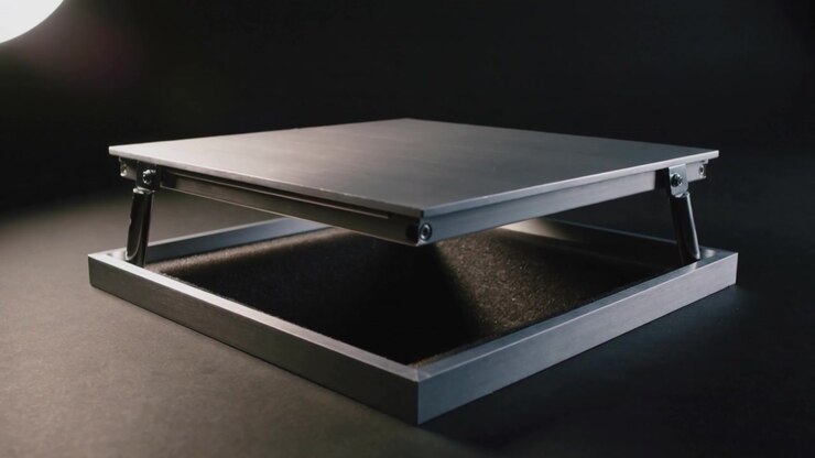 Lifting metal platform gas-strut arms extending as hinges engage at studio table