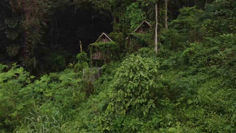 forward dolly shot drone, of old style wooden thai bungalows that are now derelict and unused being reclaimed by the jungle due to the effects of the pandemic on travel and tourism