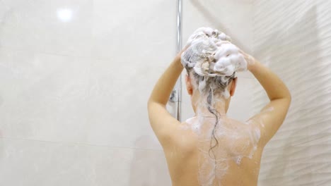 a girl who instantly washes her long hair with shampoo while standing under the shower in the bathroom.