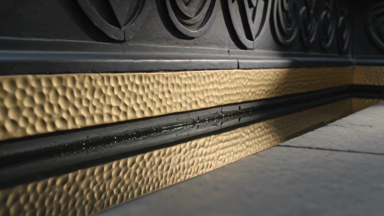 Moving low-angle camera shifting right along hall base, showing hammered gold strip, beads, frieze