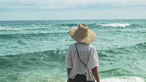 a woman with a big straw hat enjoys a walk by the sea