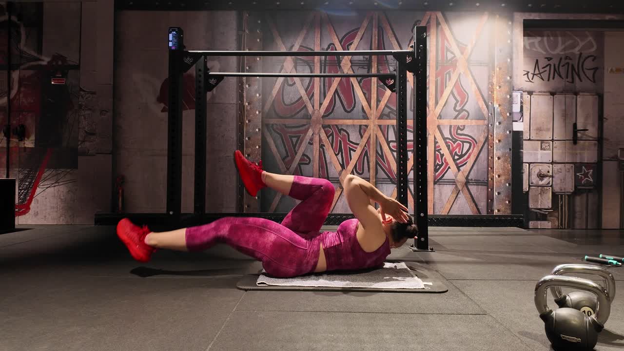 Side profile of a fit woman performing bicycle crunches on a mat. She is strengthening her core and oblique muscles as part of a dedicated fitness routine in a gym