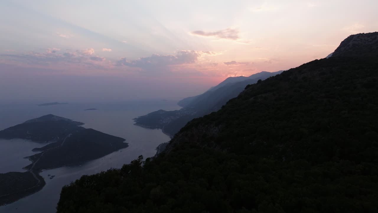 Dusk falls over Kas, Antalya, highlighting the coastal mountains and the tranquil atmosphere, silhouette of mountains with light rays breaking through clouds
