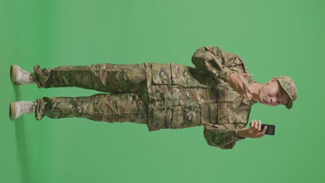 full body of asian man soldier waving hand having a video call on smartphone while standing in the green screen background studio