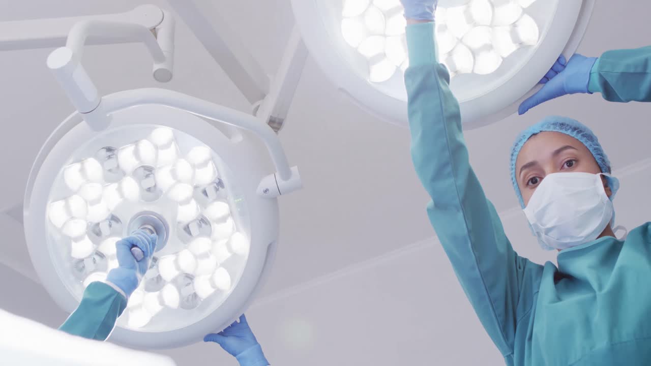 Plano contrapicado de asistenta quirúrgica mestiza preparando las luces en quirófano, espacio para texto.