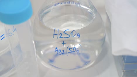 flask container with transparent liquid and chemical formulas in a laboratory