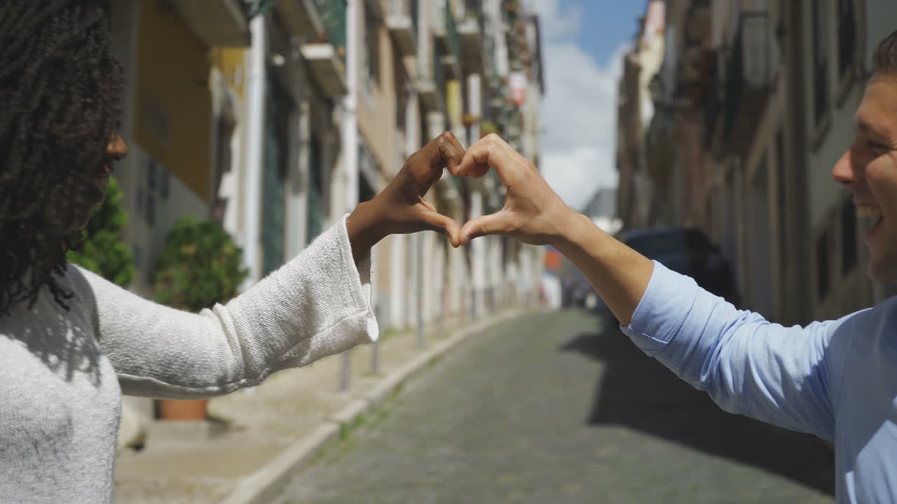 una pareja de jóvenes sonrientes haciendo forma de corazón con las manos.