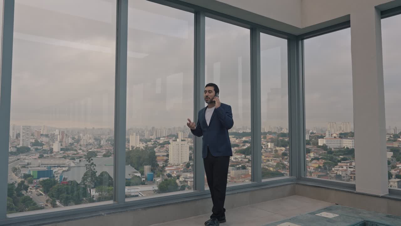 Executive man talking on the phone on the terrace of the building with city skyline in the background. Zoom out.