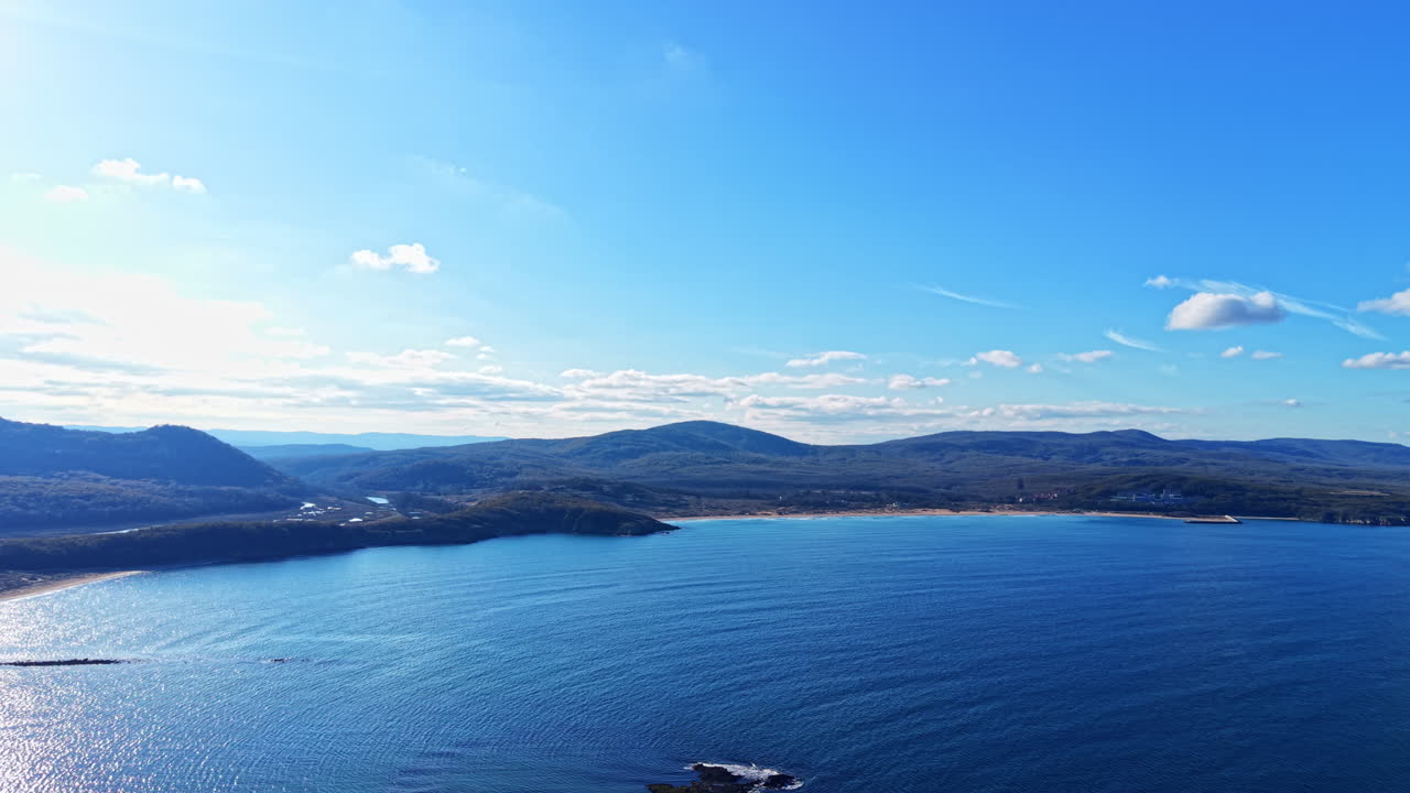 Breathtaking coastal view captures shimmering waters and majestic hills under a clear blue sky during a peaceful afternoon