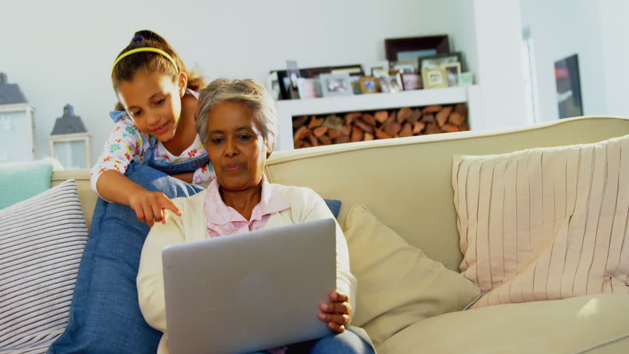 Grandmother and granddaughter using laptop in living room 4k