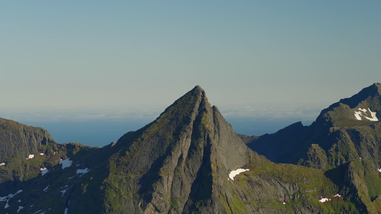 Inquadratura statica di una ripida cima di granito nelle Lofoten, Norvegia, con ampie viste sull'oceano e cieli blu, che cattura un paesaggio montano nordico drammatico e sereno