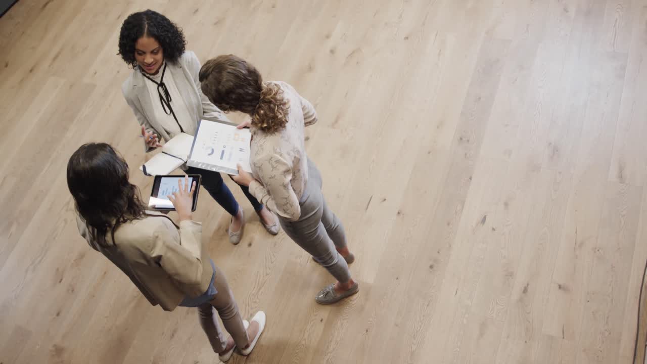 Diverse female colleagues in discussion using tablet in office lounge, slow motion